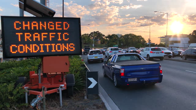 Illuminated LED construction sign notifying drivers on a busy road of changed traffic conditions due to road construction ahead at sunset