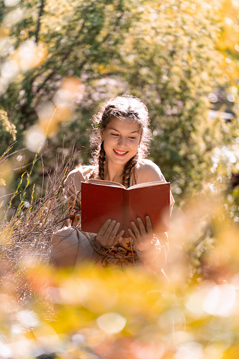 Young woman smiling while enjoying reading a book outdoors in the nature.