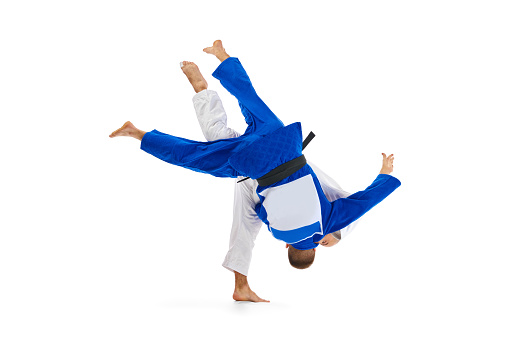 Two male professional sportsmen during match. Judo fighter attacking his opponent with leg technique isolated white background. Concept of martial art, combat sport, health, energy, fit. Copy space