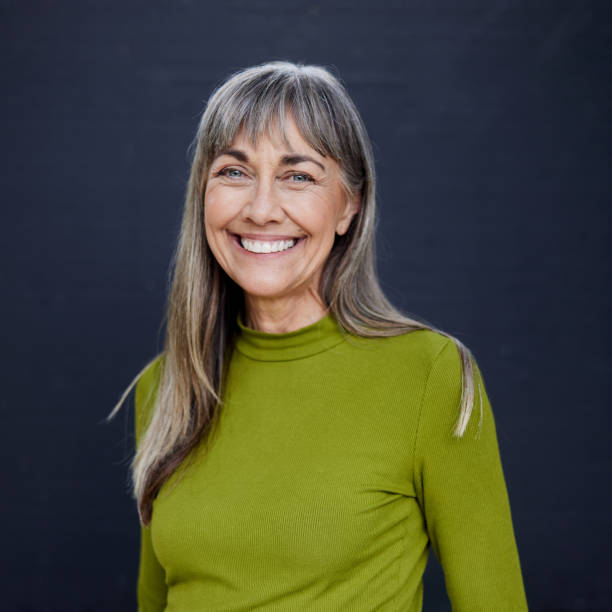 Mature woman smiling while standing in front of a dark background