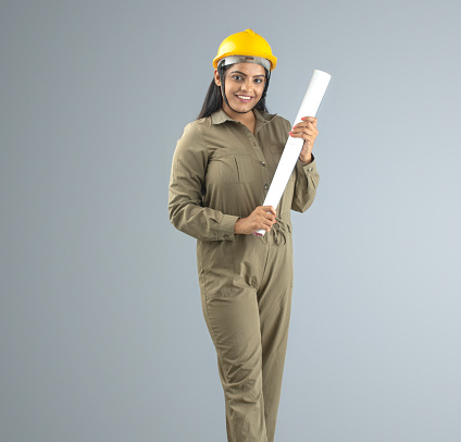 Portrait of smiling female engineer holding blueprint while standing on gray background