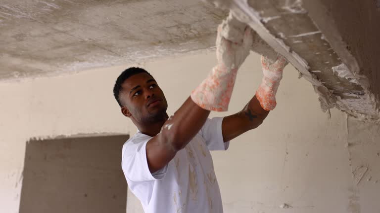 Black worker at a construction site plastering a wall with a big spatula