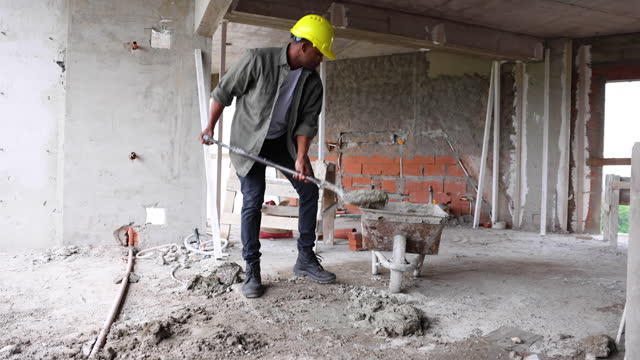 African American construction worker preparing cement with a shovel and putting it in a wheelbarrow at a construction site