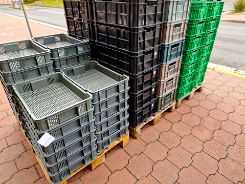 stacks of vegetable crates and other storage are on the pavement in front of a home improvement store. warehouse yard of a food company with plastic boxes stacked palet jack, bayrampasa, box shape, reuse