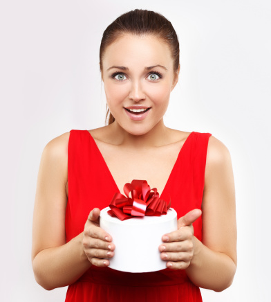 Happy young woman holding gift, laughing and looking at camera