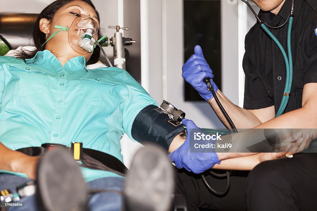 Paramedic with patient on stretcher Paramedic assisting a woman (30s, Hispanic) lying on a stretcher. Blood Pressure Gauge Stock Photo