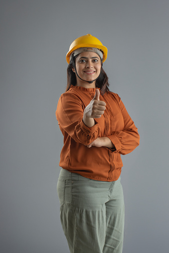 Portrait of confident female engineer showing thumbs up sign while standing on gray background