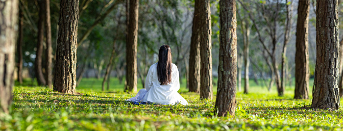 Woman relaxingly practicing meditation in pine forest to attain happiness from inner peace wisdom with beam of sun light for healthy mind and soul for healthy mind and soul