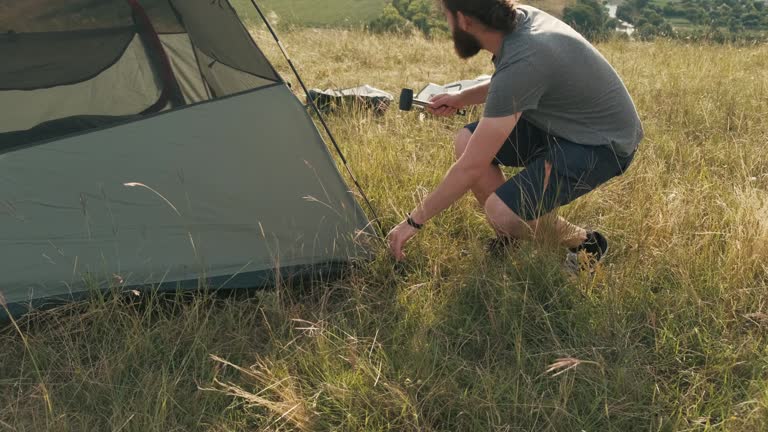 Young bearded man installing camping tent for comfort night.