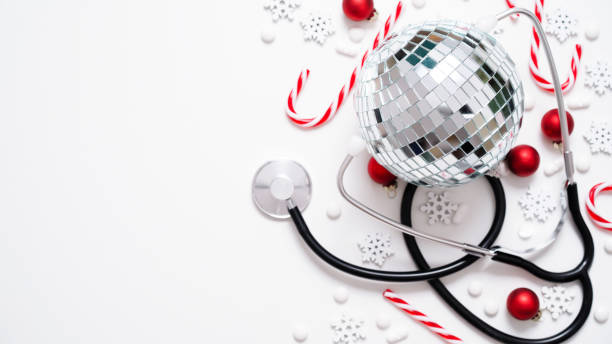 Christmas medical banner.Close-up of stethoscope,disco ball,striped lollipops,red balls,stars and pills on white background,top view,flat lay,copy space.New Year's medicine, congratulations to doctor banner médico navideño. primer plano del estetoscopio, bola de discoteca, piruletas rayadas, bolas rojas, estrellas y píldoras sobre fondo blanco, vista superior, plano plano, espacio de copia. medicina de año nuevo, felicitaciones al médico.