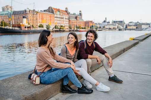 Three young friends sitting on the quayside in Malmo in Sweden.