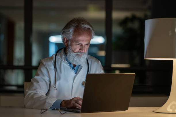 um médico do turno da noite examina um caso em um laptop em um consultório escuro - doctors office examination table medical exam clinic - fotografias e filmes do acervo