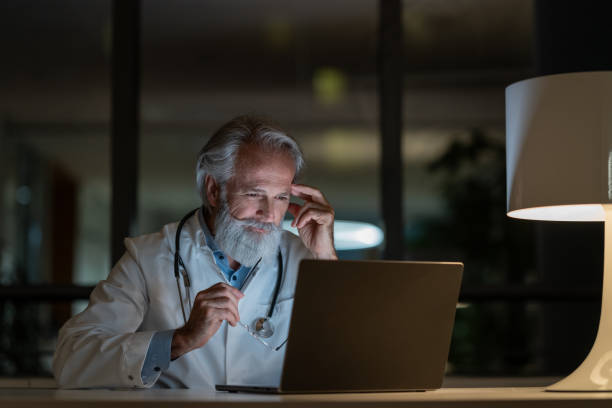 um médico do turno da noite examina um caso em um laptop em um consultório escuro - doctors office examination table medical exam clinic - fotografias e filmes do acervo