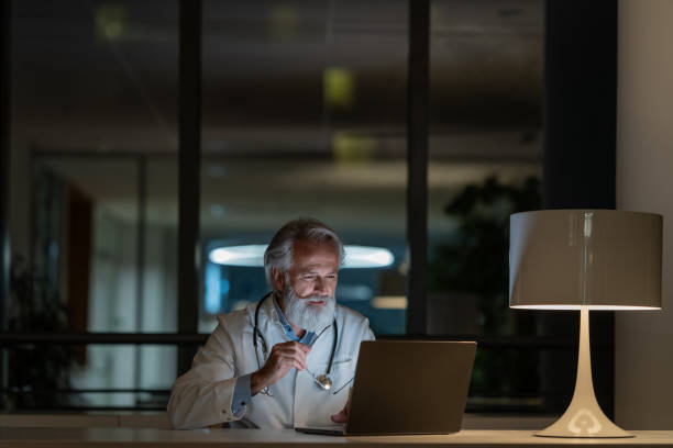 lekarz nocnej zmiany bada przypadek na laptopie w zaciemnionym biurze - doctors office examination table medical exam clinic zdjęcia i obrazy z banku zdjęć