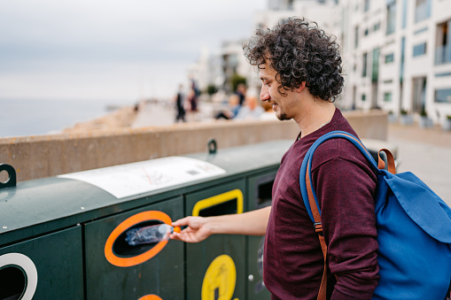 Young man putting a water bottle in a recycling bin in Malmo in Sweden.
