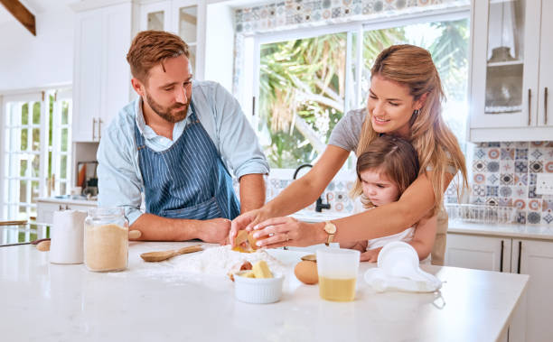 baking, child and parents teaching a child to bake in the kitchen of a house. cooking, happy and mother and father helping a girl kid learning to make a cake, food or breakfast in their family home - domestic life young family family child imagens e fotografias de stock