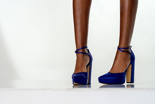 A close-up of a woman's legs in blue high heel shoes, on a white surface