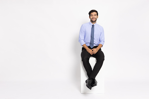 Young businessman sitting on white box and smiling isolated on white background