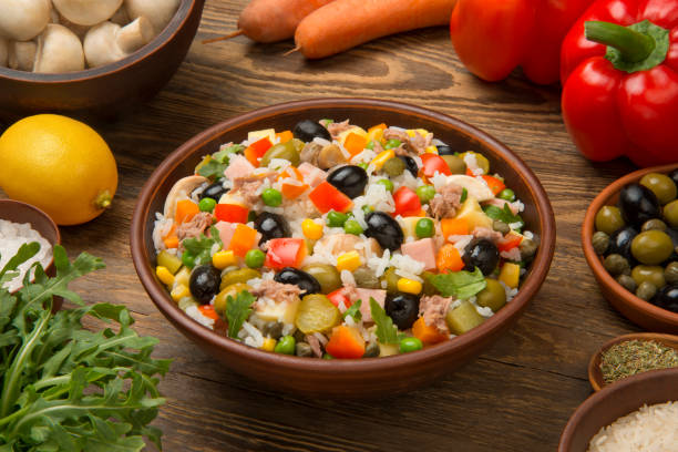 Italian rice salad with tuna in a brown ceramic salad bowl on a rustic wooden table with ingredients. stock photo