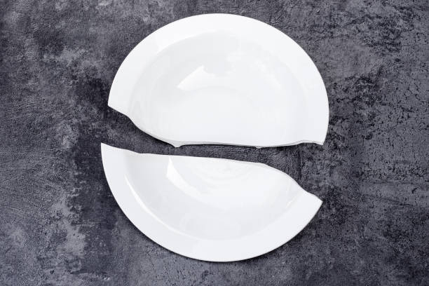 Two halves of a white plate broken in half on a dark surface with a concrete texture. Concept of rupture, collapse, misfortune.