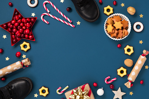 Saint Nicholas Day, 6 December. Christmas card with children's shoes, sweets, candy, gingerbread cookies, gifts on blue background, top view. Traditional winter holiday in Germany and Western Europe.