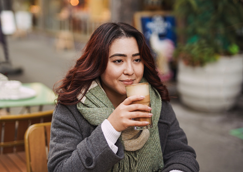 Young asian woman drinking hot coffee druing winter time outside of vintage restaurant - Multiracial person enjoy day in the city