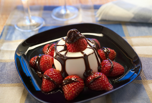 sweet pannacotta with caramel and strawberries served in black plate on table