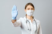 Doctor wearing medical face mask and disposable gloves showing stop gesture