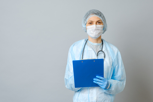 Young woman physician with stethoscope prescribing treatment to patient. Female doctor with pen writing recipe on clipboard. Isolated on gray