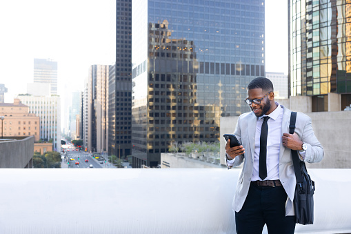 Pleasant Young Multi-Ethnic Bearded Man Typing On The Phone With City View In the Background. Concept of using technology and commuting the city.