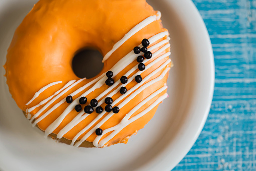 Bright orange donut decorated with glaze and chocolate balls on a blue wooden background, top view.