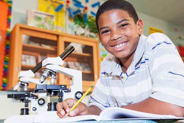 Boy using microscope African American boy (9 years) in science class using microscope. biology class stock pictures, royalty-free photos & images