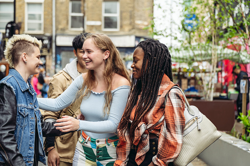 Group of diverse friends meet up at Brick Lane putting arms around each other to say hello.