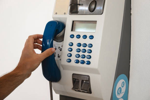 old public telephone for making voice calls using coins or prepaid card stuck on a white wall. person's hand holding handset to make a call. - coin operated pay phone telephone communication imagens e fotografias de stock