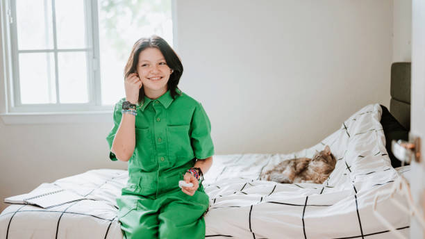 Transgender non binary teenager hanging out at home in bedroom with pet cat listening to music with joy stock photo