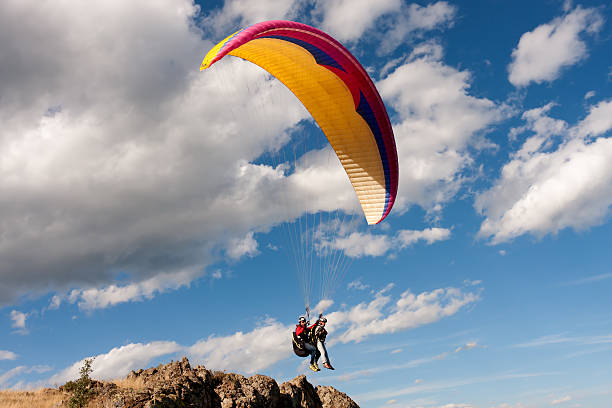 Tandem paraglider starting a flight Tandem paraglider in a moment of take off. The team jumps off a rocky cliff in a beautiful spring day. The wind conditions are perfect for flying. The sky is blue, the atmosphere is crisp with few clouds around, making the landscape even more picturesque. paraglider stock pictures, royalty-free photos & images