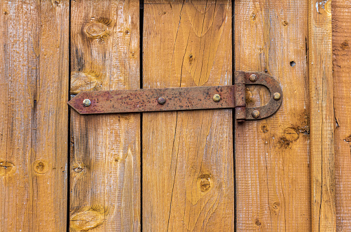 A rusty antique door hinge bolted to a painted wooden door