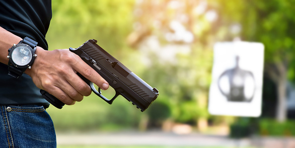 Gun shooter holding semi automatic 9mm pistol gun with blurred target shooting rage background, concept for protection humans property and humans life by using weapon.