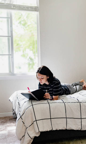 istock Transgender non binary teenager writes or draws in notebook or diary lying on their bed at home in concentration 1796775874