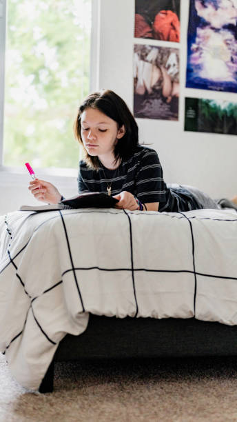 istock Transgender non binary teenager writes or draws in notebook or diary lying on their bed at home in concentration 1796775876