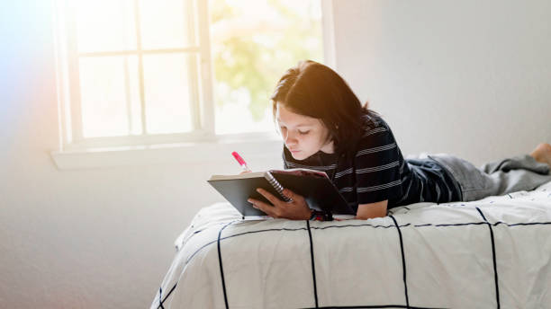istock Transgender non binary teenager writes or draws in notebook or diary lying on their bed at home in concentration 1796778110