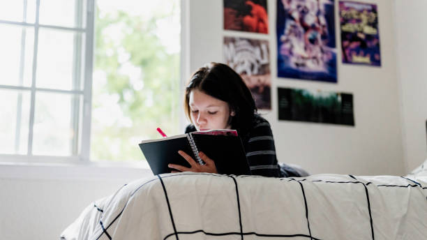 istock Transgender non binary teenager writes or draws in notebook or diary lying on their bed at home in concentration 1796778310