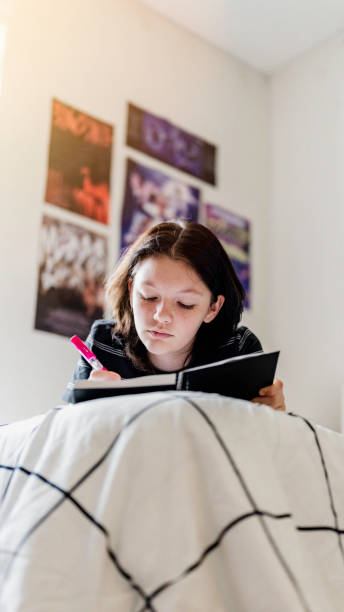 istock Transgender non binary teenager writes or draws in notebook or diary lying on their bed at home in concentration 1796781922