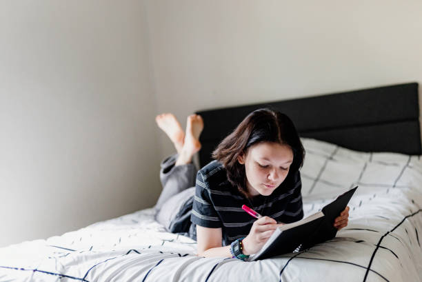 istock Transgender non binary teenager writes or draws in notebook or diary lying on their bed at home in concentration 1796785220