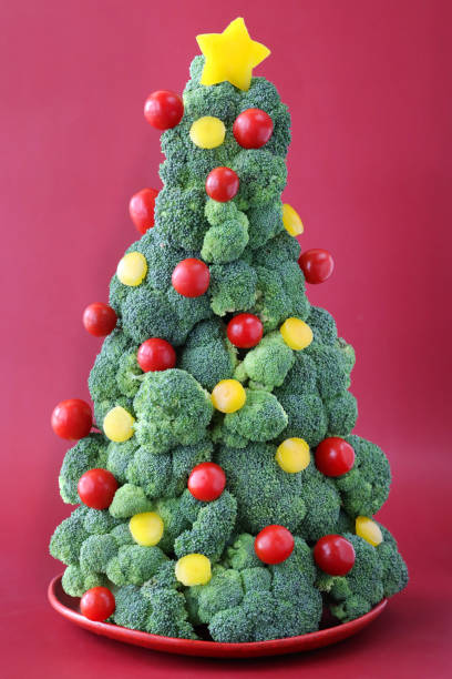istock Close-up image of broccoli Christmas tree buffet centrepiece, yellow bell pepper and red cherry tomato baubles, red background, focus on foreground 1796785796