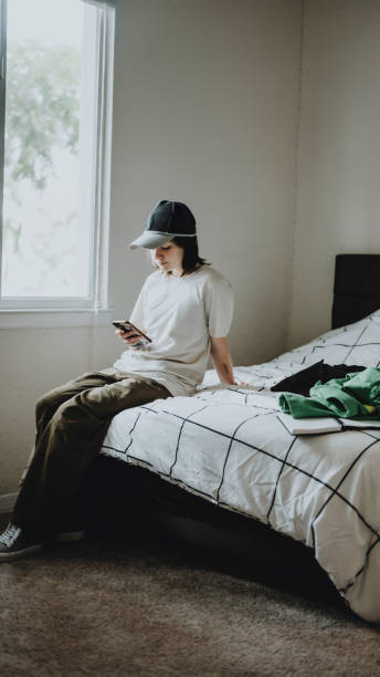 Transgender non-binary teenager at home in their bedroom using cellphone stock photo