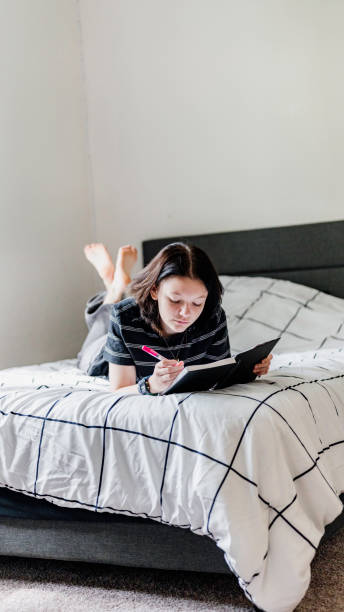 istock Transgender non binary teenager writes or draws in notebook or diary lying on their bed at home in concentration 1796787311