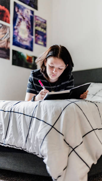istock Transgender non binary teenager writes or draws in notebook or diary lying on their bed at home in concentration 1796787373