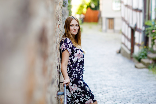Beautiful young woman with long hairs in summer dress going for a walk in German city. Happy girl enjoying walking in cute small fachwerk town with old houses in Germany