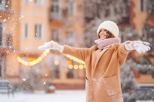 A sweet woman walks along a decorated street on a winter day. Curly woman enjoying snowfall, winter holidays outdoors. Holidays concept.